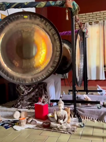 Gongs y estatua de Buda en una habitación con una caja roja, probablemente para un baño de sonido o meditación.