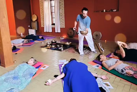 Personas tumbadas sobre colchonetas de yoga en una habitación mientras alguien toca un cuenco