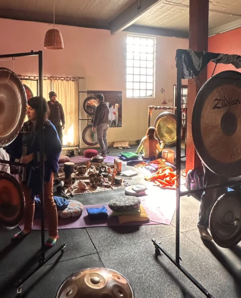 Personas en una habitación con gongs y cojines, probablemente para un baño de sonido.