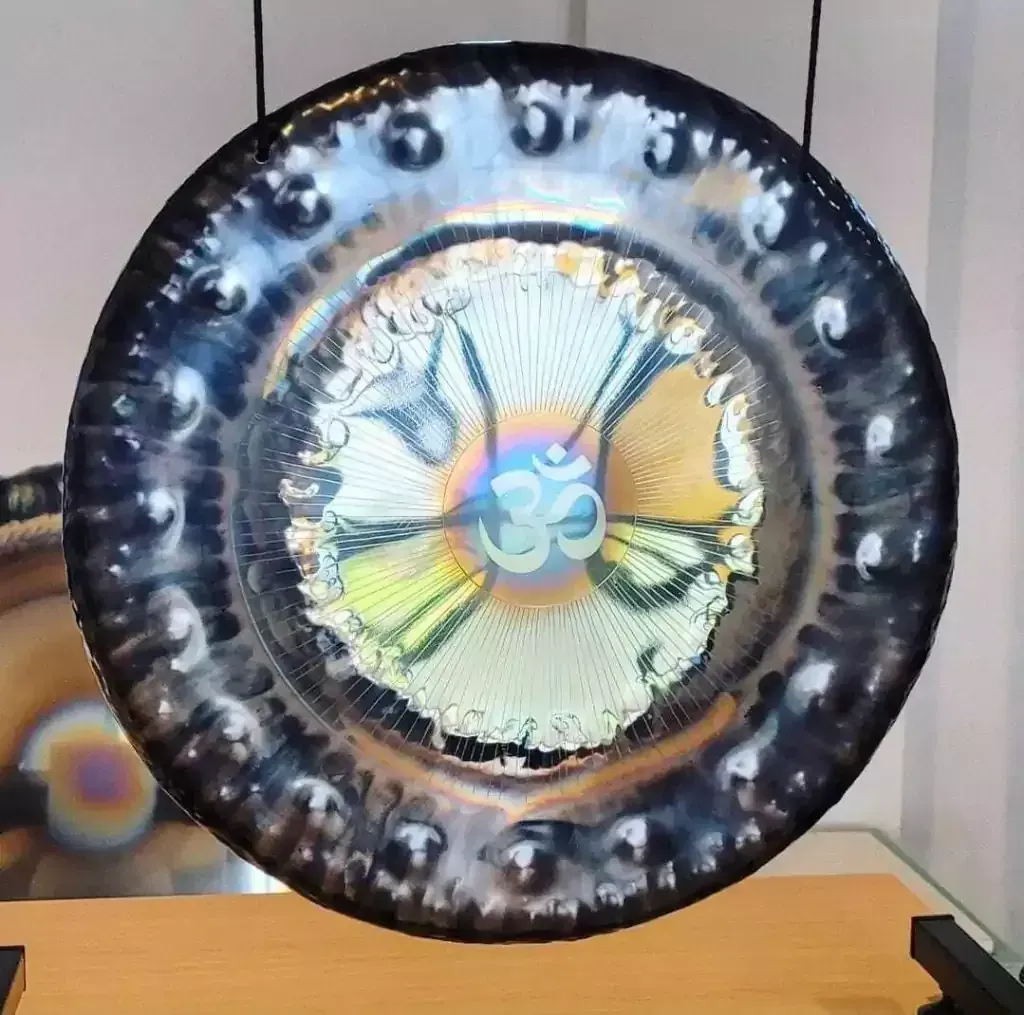 Gong metálico grande y redondo con superficie reflectante e iridiscente. El símbolo Om está en el centro.