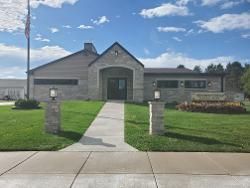 Single-story stone building with a central walkway, green lawn, and blue sky