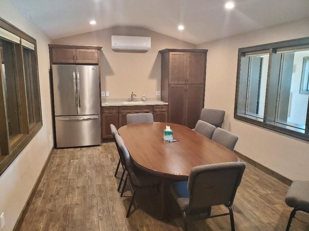 Small dining room with wooden table, four chairs, stainless fridge, and wall-mounted AC unit