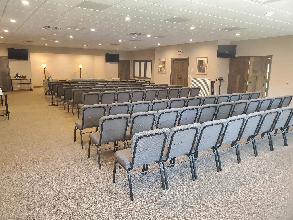 Empty conference room with rows of gray chairs facing a front stage and podium under bright ceiling lights