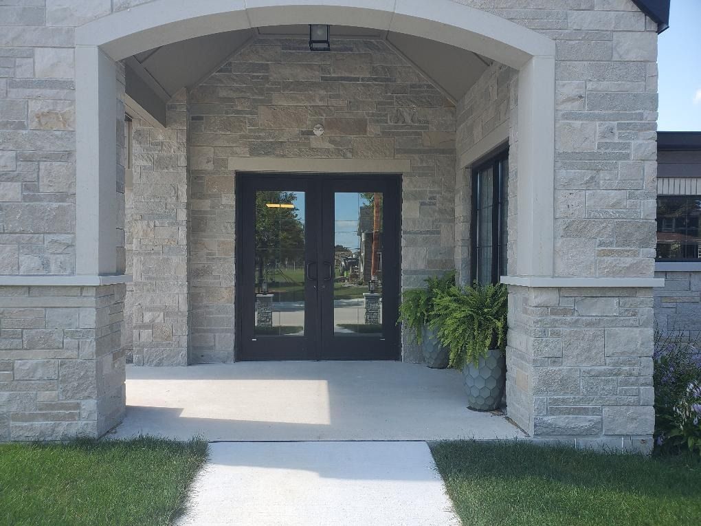 Stone building entrance with arched porch, glass double doors, and a potted plant beside the doorway