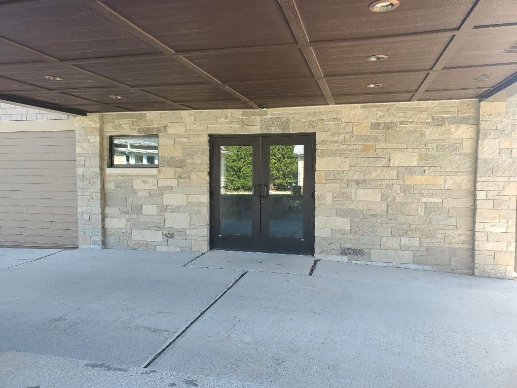Building entrance with dark glass doors, stone facade, and covered concrete walkway