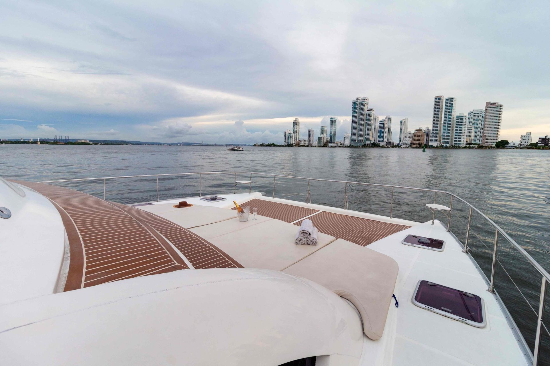 A catamaran on the water with a city skyline in the distance, cloudy sky overhead.