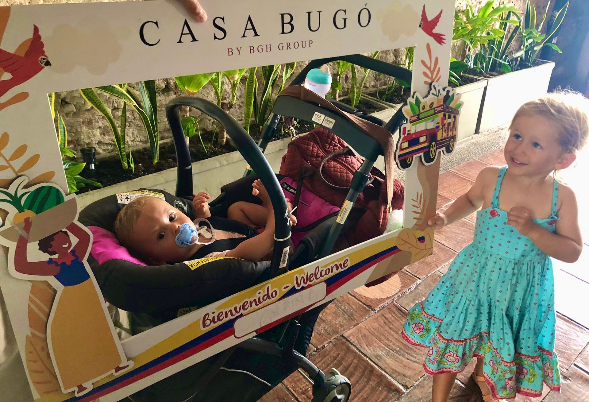 A baby in a car seat framed by a decorative sign that says