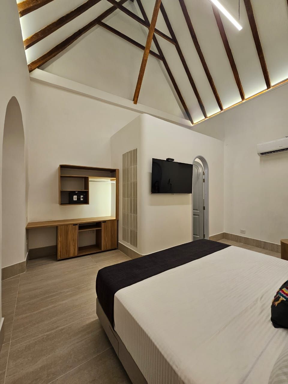 Un dormitorio con una cama grande y un televisor de pantalla plana en la pared.
