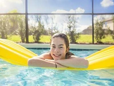 Person resting on a yellow pool float, smiling in a bright outdoor pool.