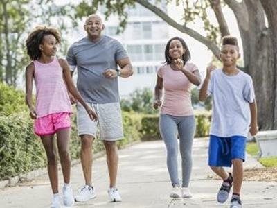 Family jogging together on a tree-lined sidewalk in a neighborhood.