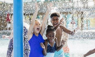 Children smiling and playing under water spray at a pool