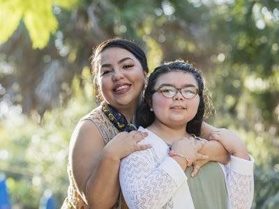 Mother and daughter smiling and hugging outdoors