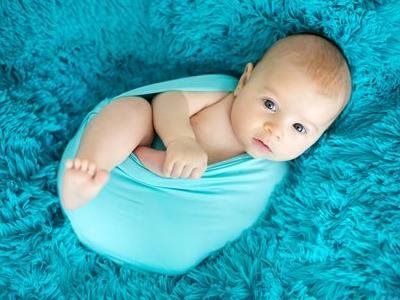 Baby wrapped in a turquoise blanket on a fluffy blue background