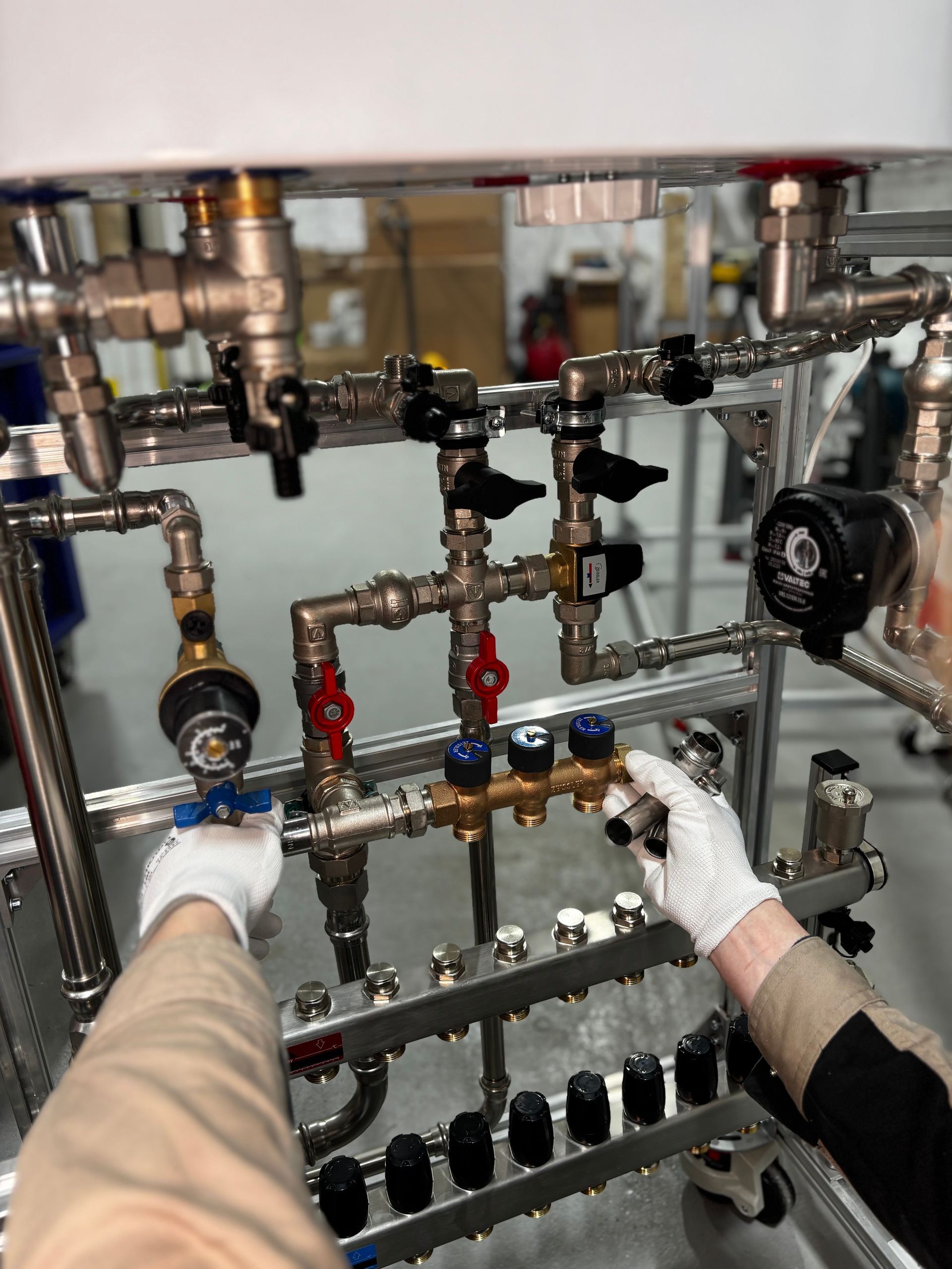 Gloved hands adjusting plumbing valves and pipes on a mechanical panel