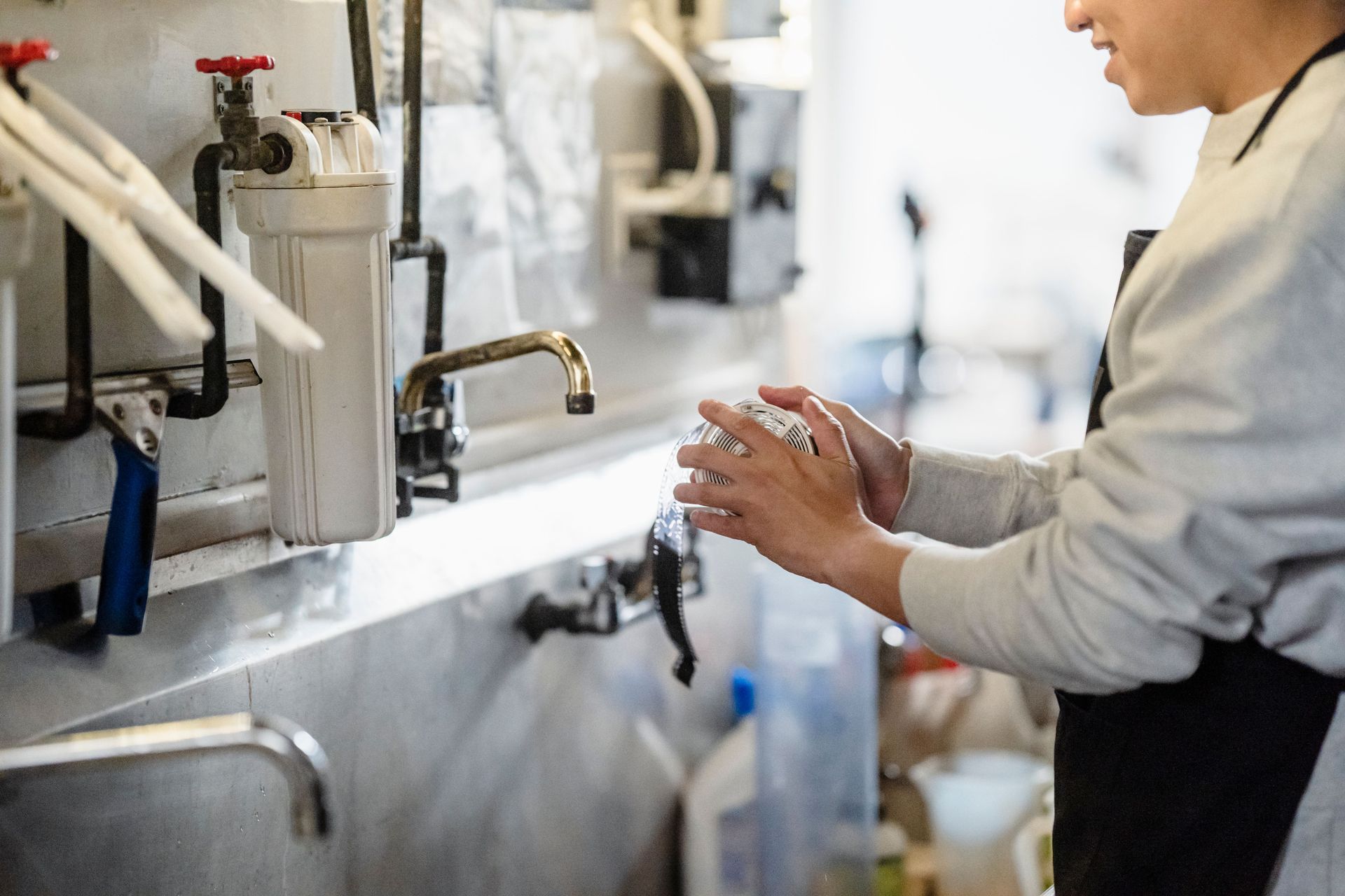 Person washing hands at a sink in a clean, stainless-steel workspace