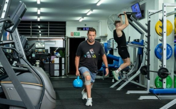 Man holding a weight in the gym and lunging. 