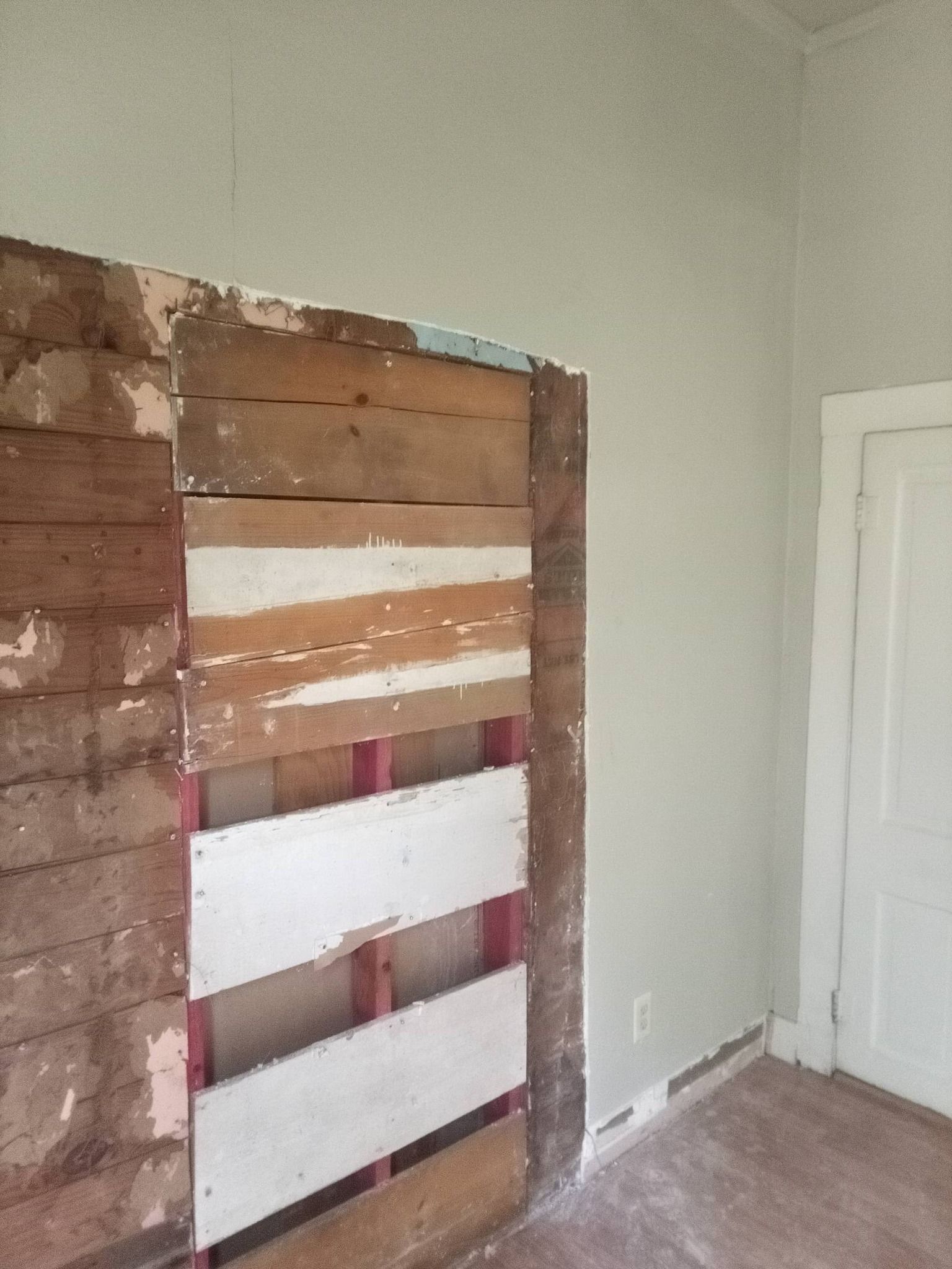 Partially dismantled wall with exposed wood and white boards in a room near a closed white door