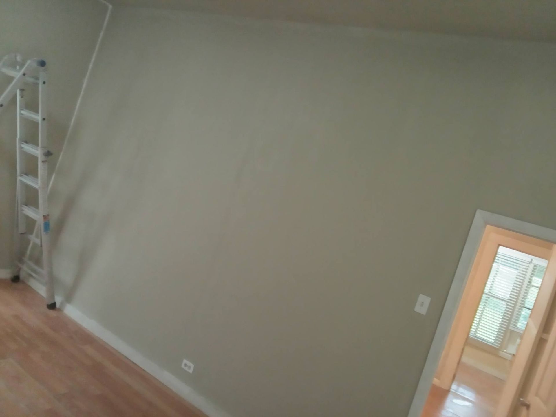 Empty room with beige walls, wood floor, and a doorway to a bright adjoining room