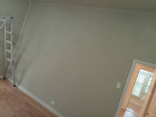 Empty room with beige walls, wood floor, and a doorway to a bright adjoining room