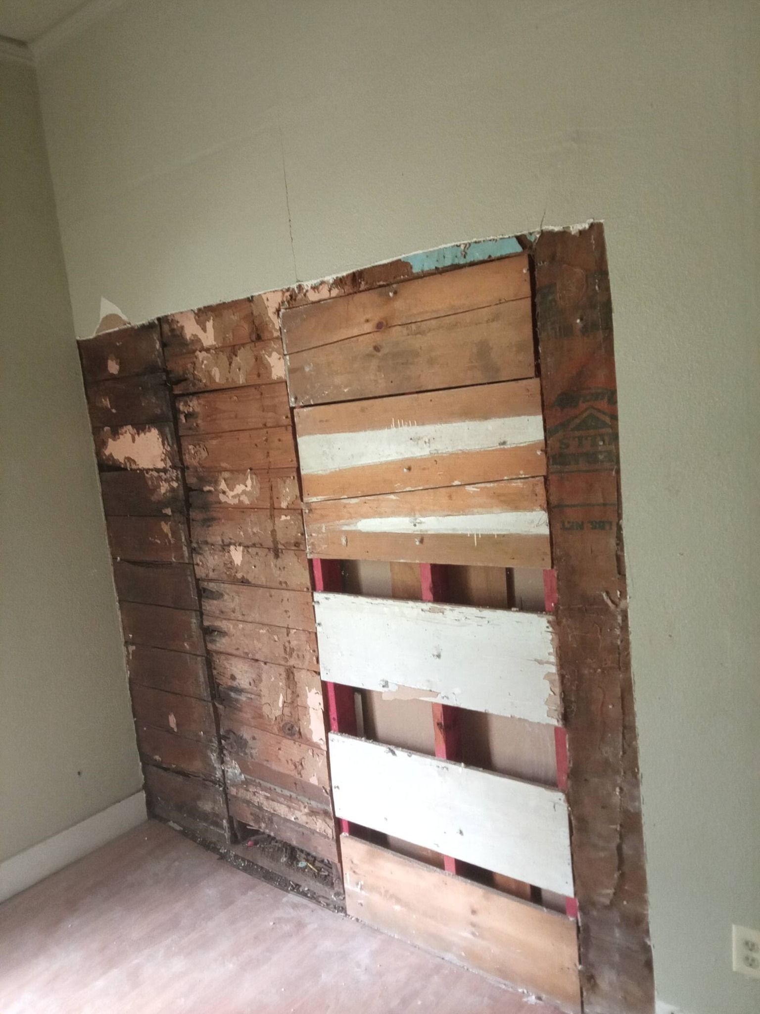 Damaged wall with exposed wood studs and torn drywall in a room corner