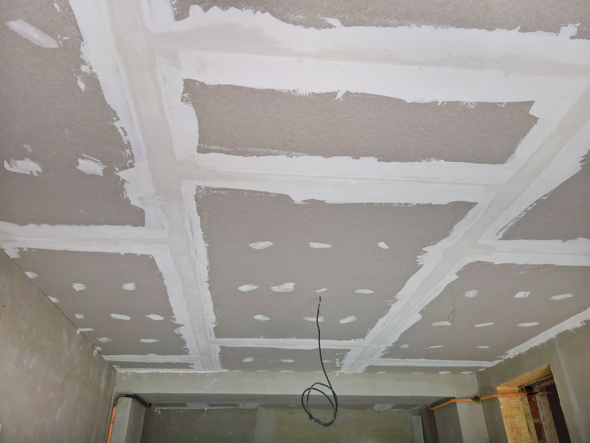 Unfinished drywall ceiling with taped seams and hanging electrical wire in a room under construction