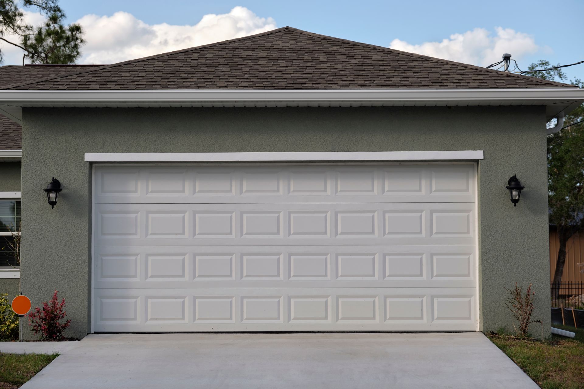 White two-car garage with a closed door on a gray house exterior.
