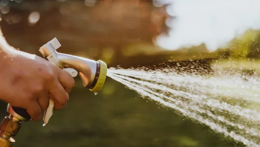 Hand holding a garden hose nozzle spraying water outdoors in sunlight
