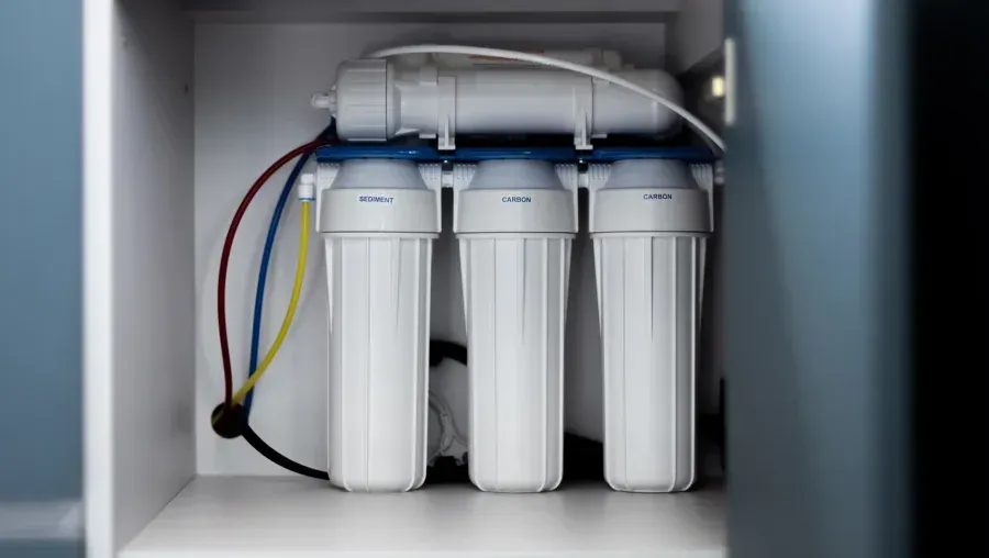Under-sink water filtration system with three white filter cartridges and connected tubes