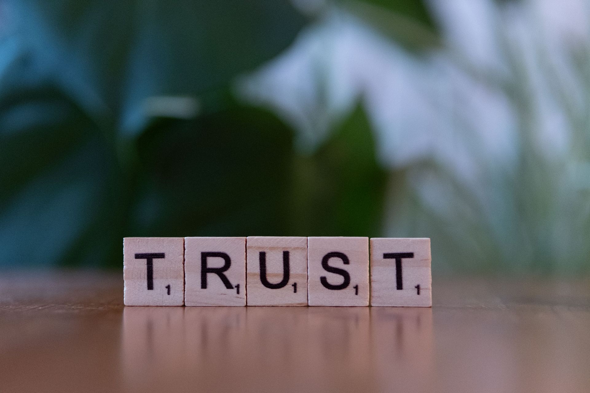 Letter tiles spelling “TRUST” on a wooden surface with a blurred green background
