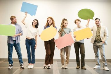 Six people in casual clothes holding colorful blank speech bubbles in a bright studio.