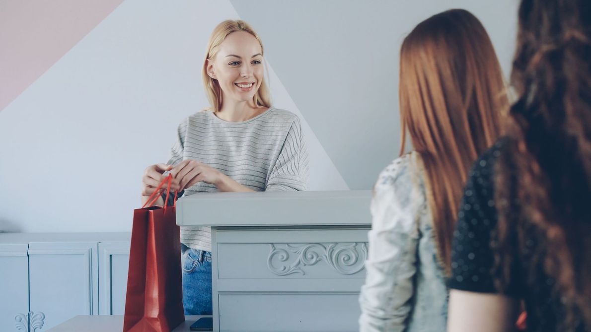 Customer at a checkout counter handing over a red shopping bag to a smiling cashier