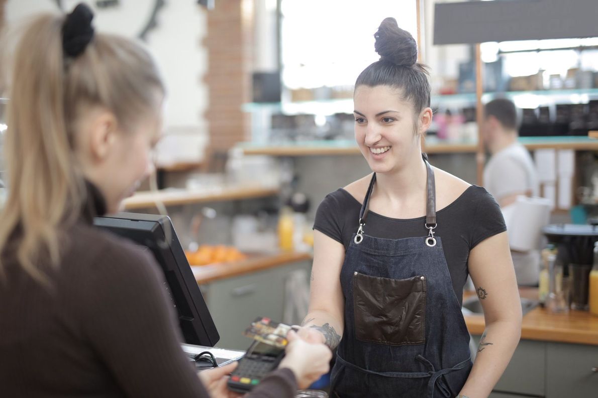 Two people exchanging a card at a café counter, with one smiling in a black apron.