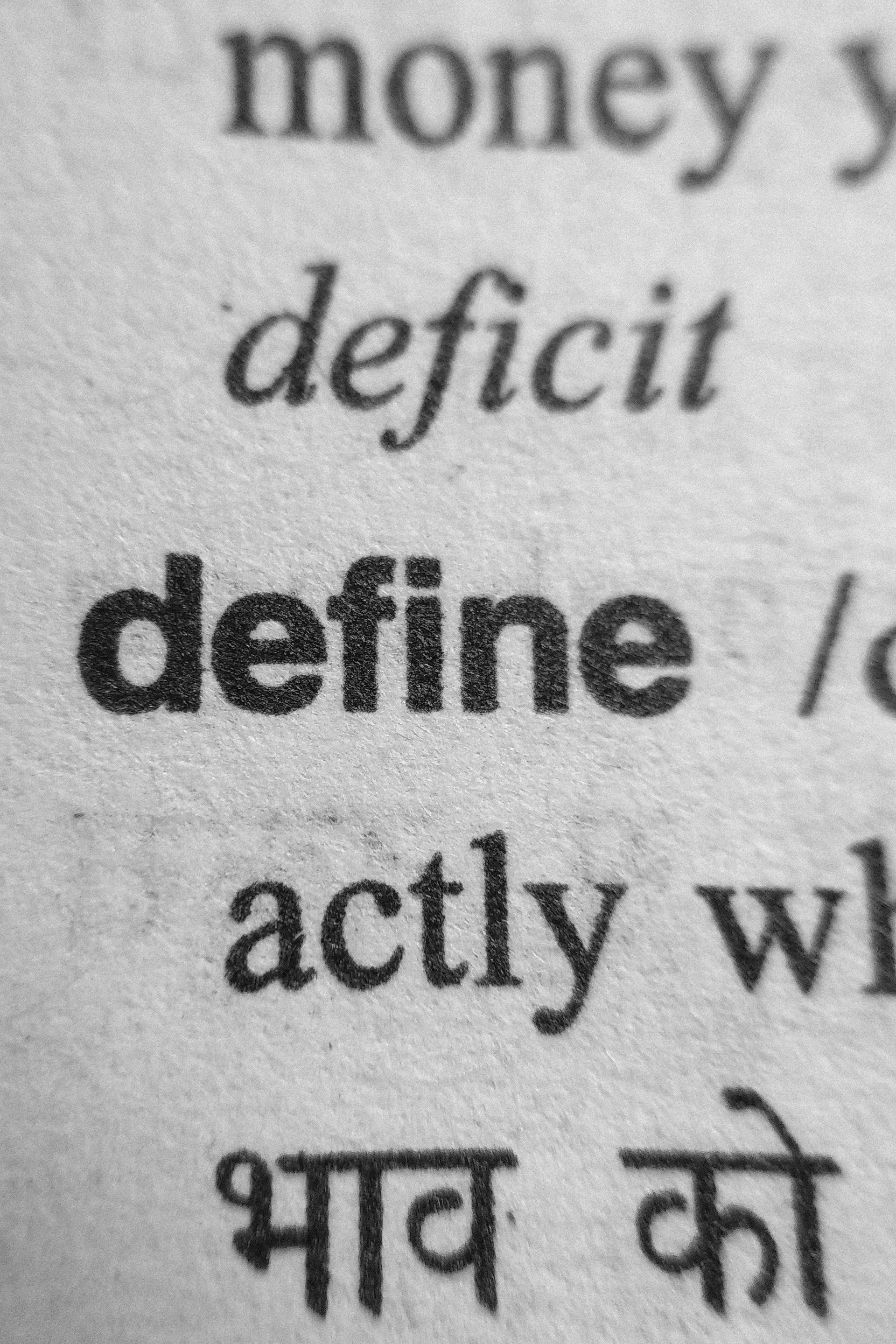 Close-up of a printed dictionary page showing the word “define” in bold, with nearby words and Hindi text.
