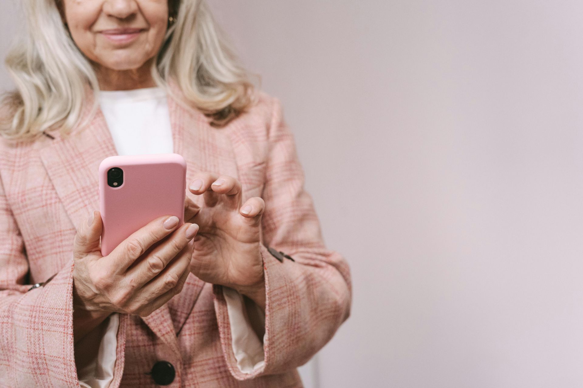 Woman in a pink blazer using a pink smartphone against a light background
