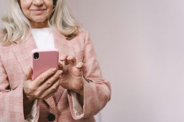 Woman in a pink blazer using a pink smartphone against a light background