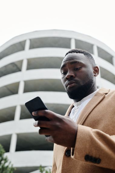 Man in tan coat looking at a smartphone in front of a curved white building