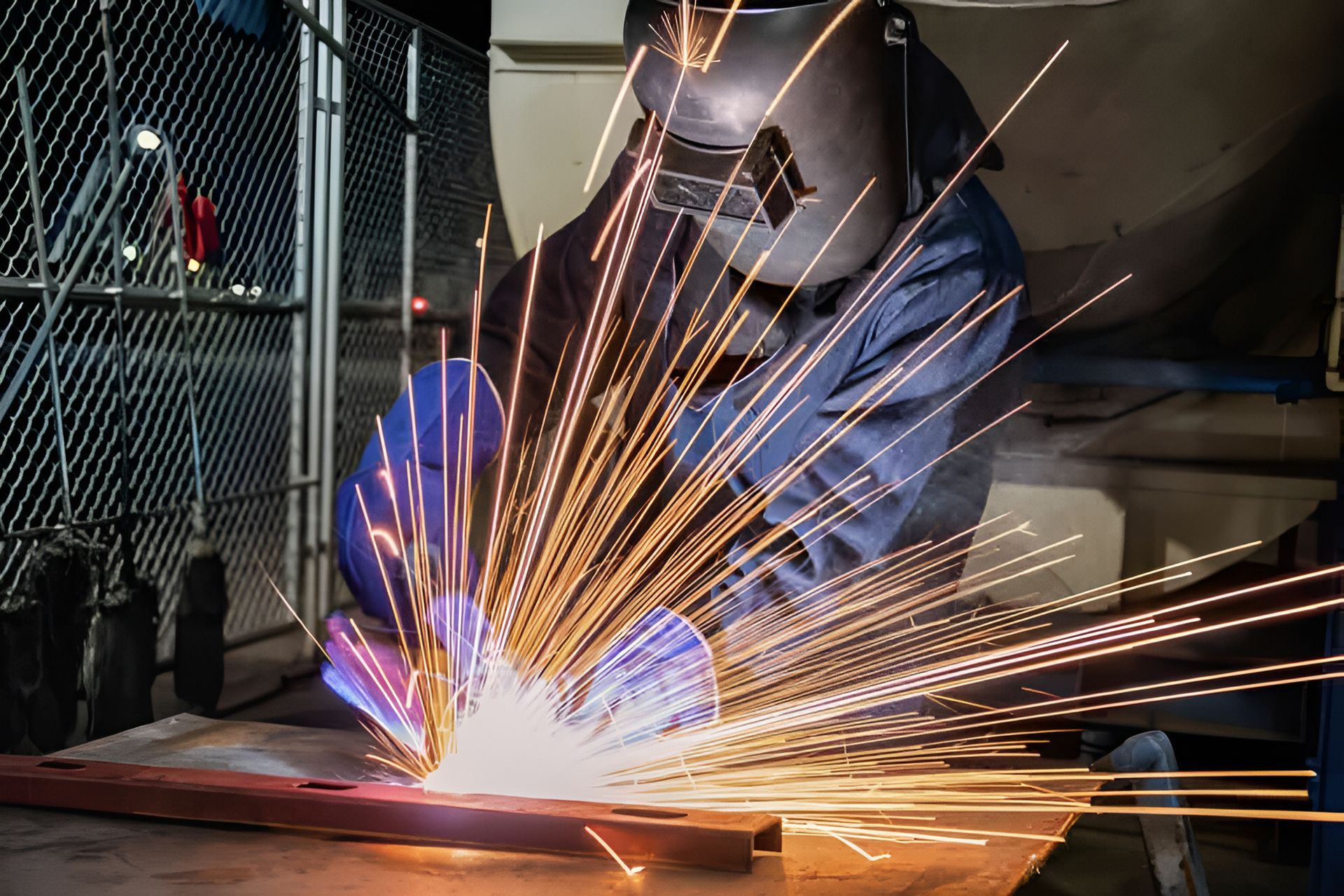 Welder in protective gear welding steel plate with sparks flying in a workshop.