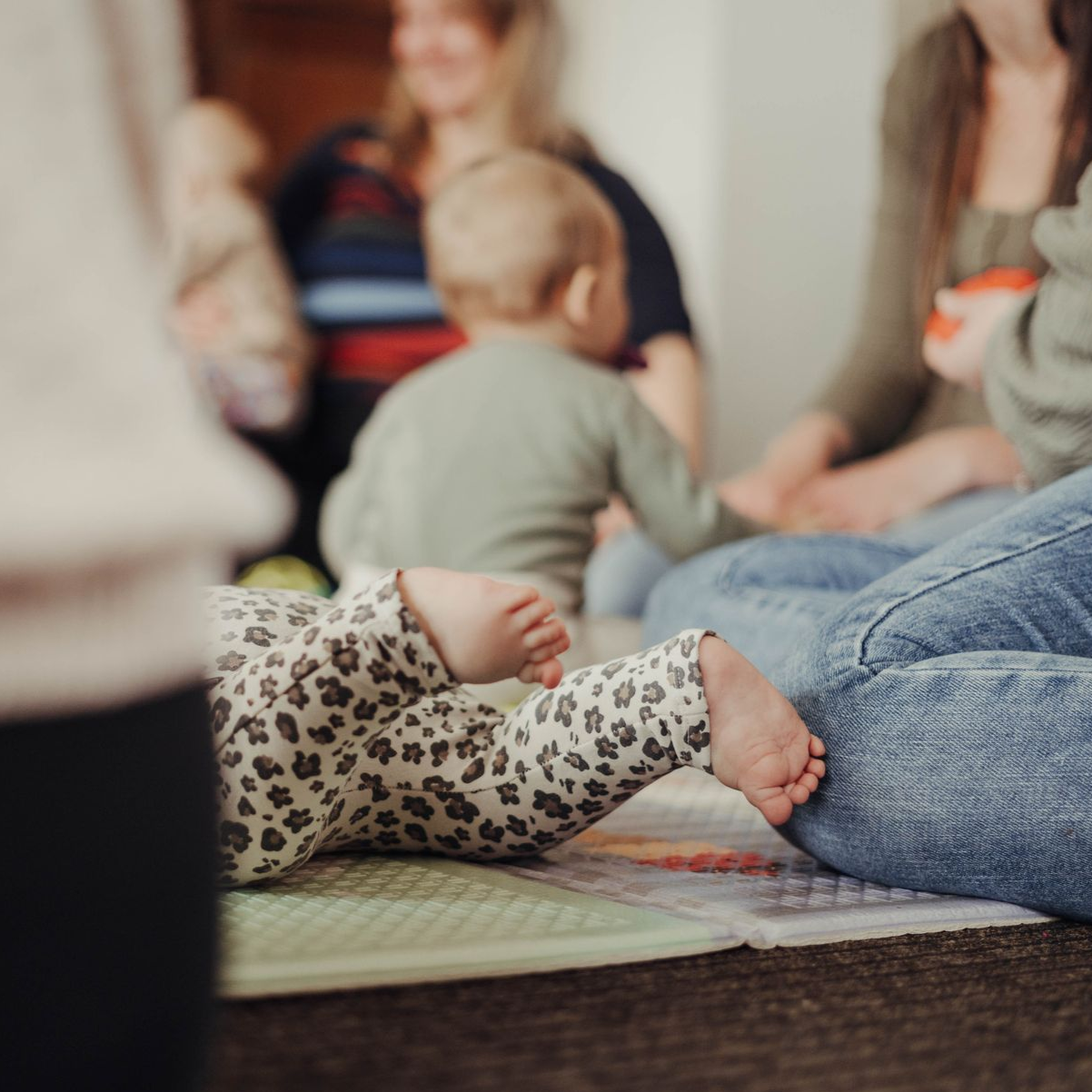 Ein Baby liegt auf einer Matte und streckt die Arme nach anderen Kindern und Erwachsenen aus. Ort: Stillcafé Grimma
