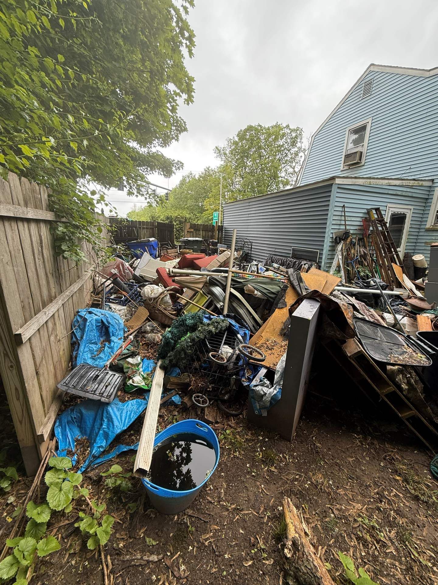 Backyard cluttered with debris; blue house in the background, cloudy sky.