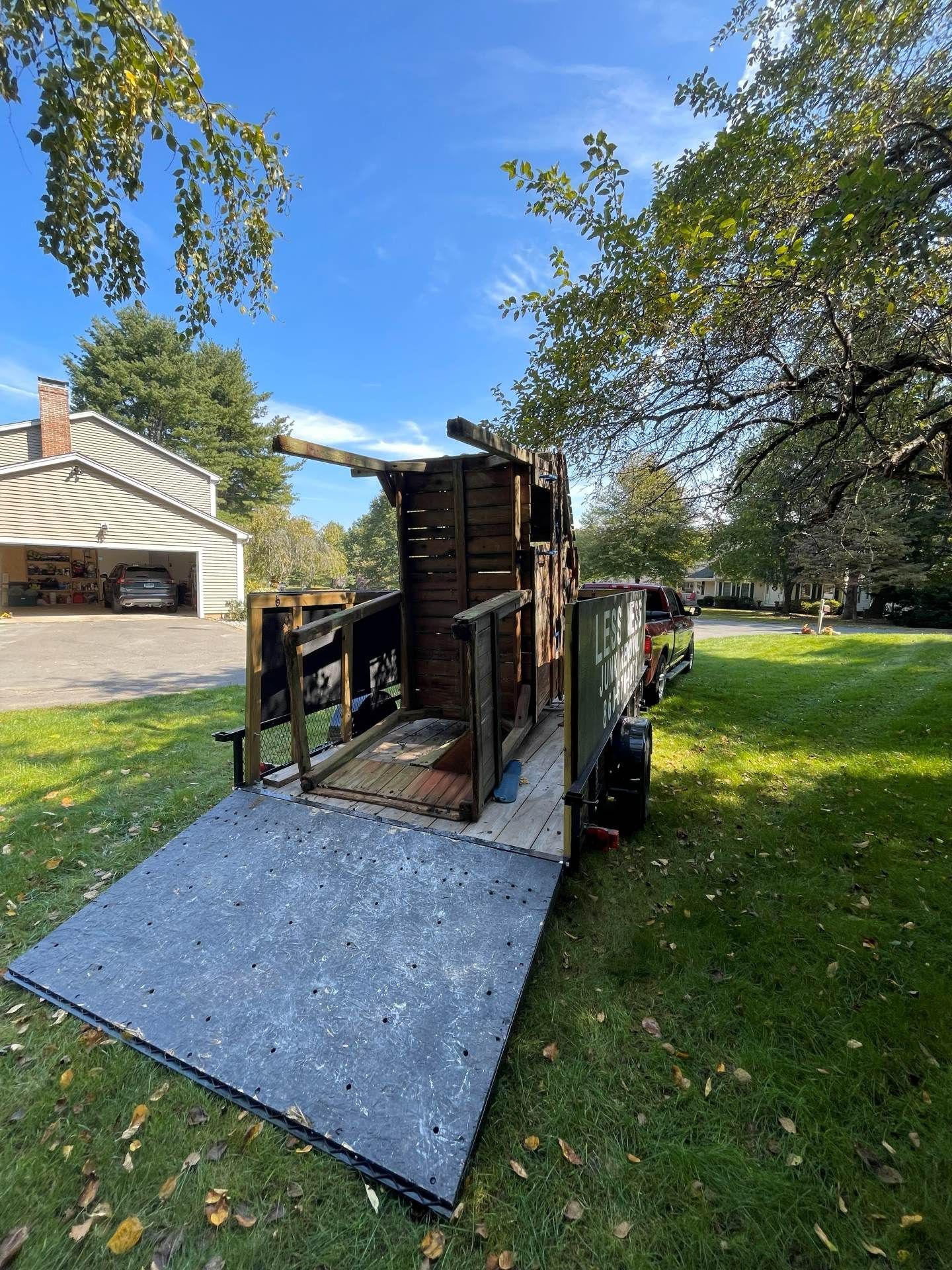 Trailer with wooden structure on a grassy lawn. Blue sky and trees in the background.