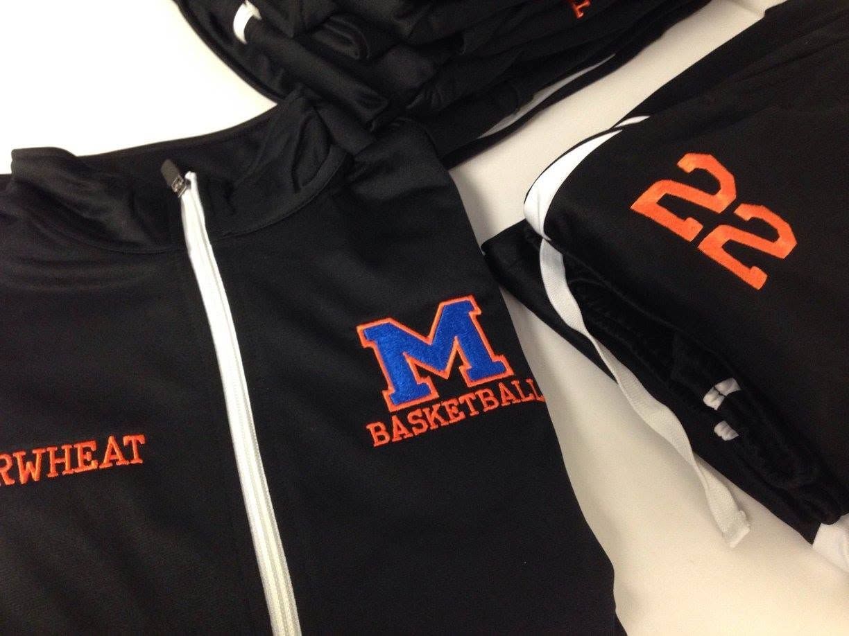 Black basketball hoodie with blue-and-orange “M” logo and orange “22” on sleeve, plus black shorts.