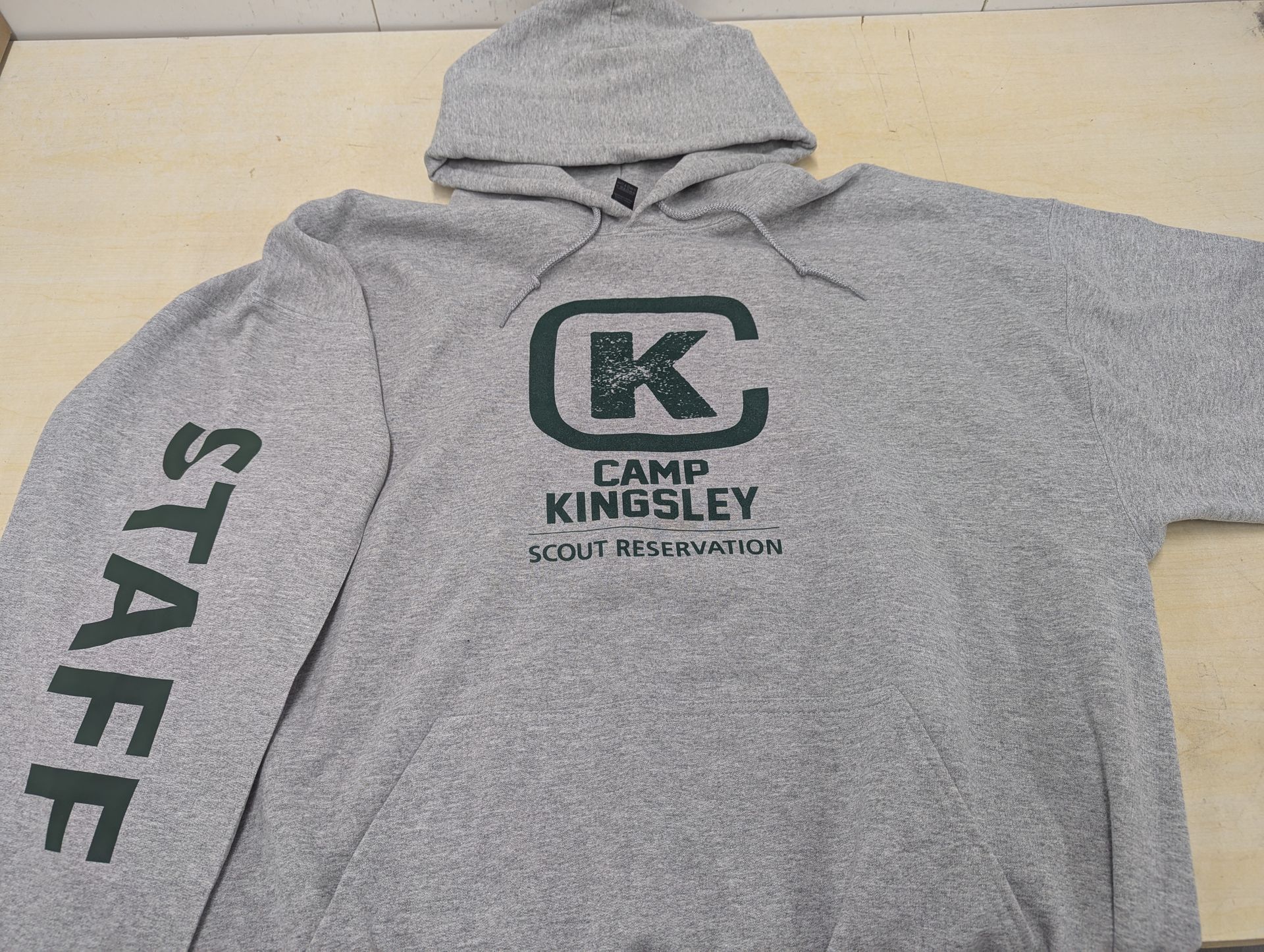 Gray hooded sweatshirt with “CAMP KINGSLEY” logo on the chest and “STAFF” printed on the sleeve.