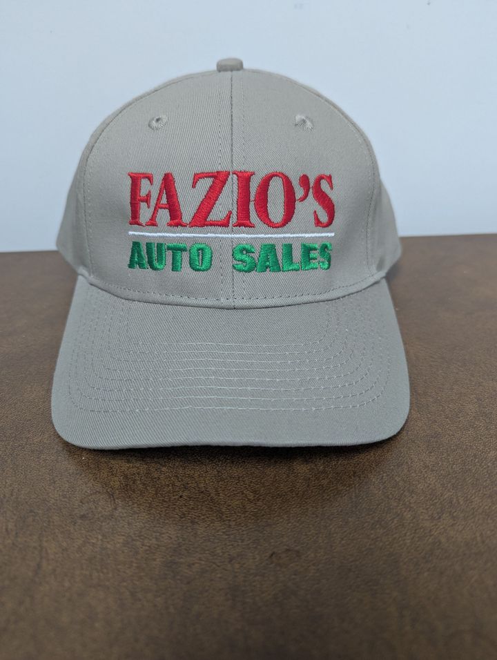 Gray baseball cap with red and green “FAZIO’S AUTO SALES” embroidery on a brown surface