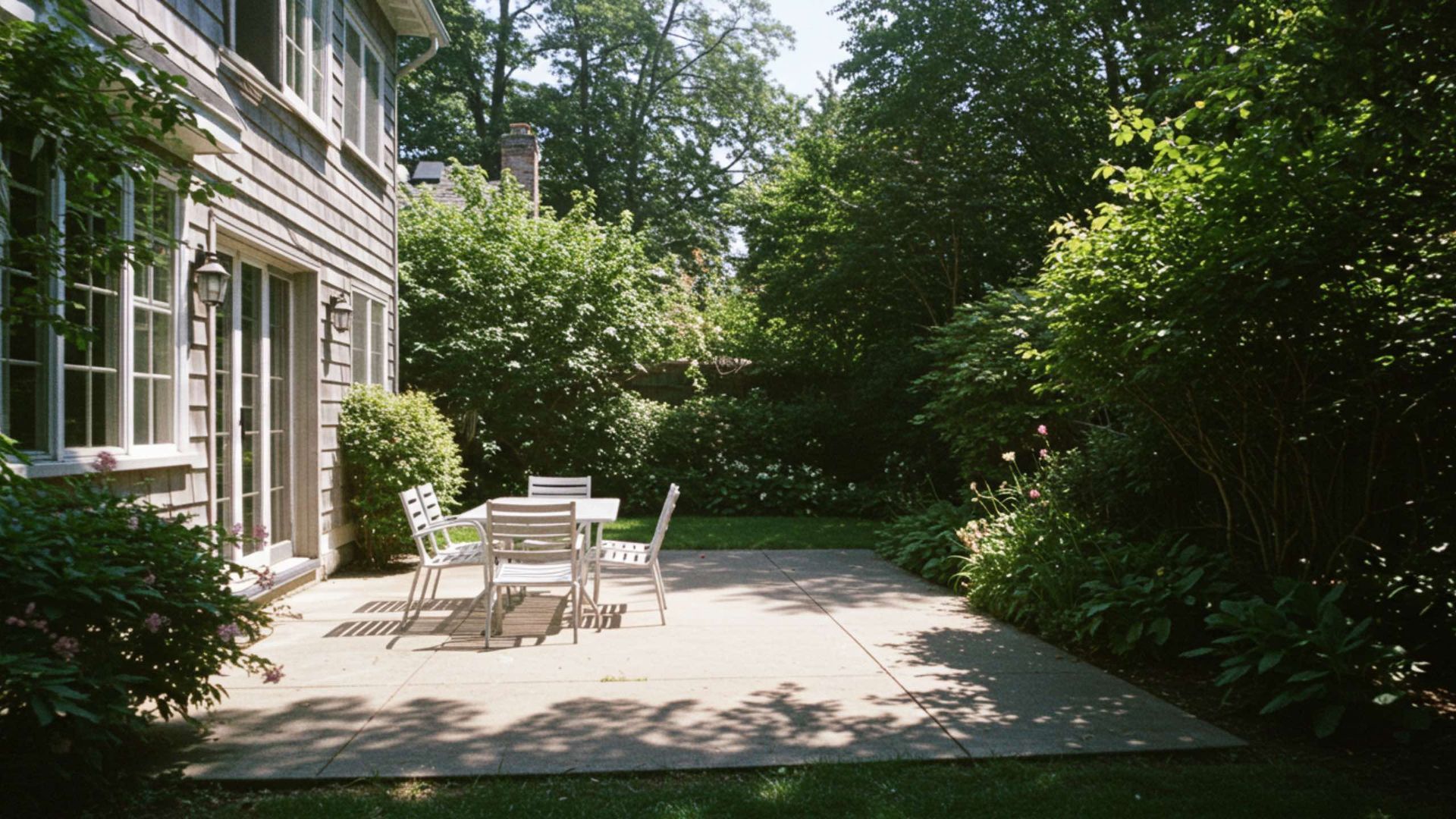 Patio with table and chairs; backyard with trees and house.