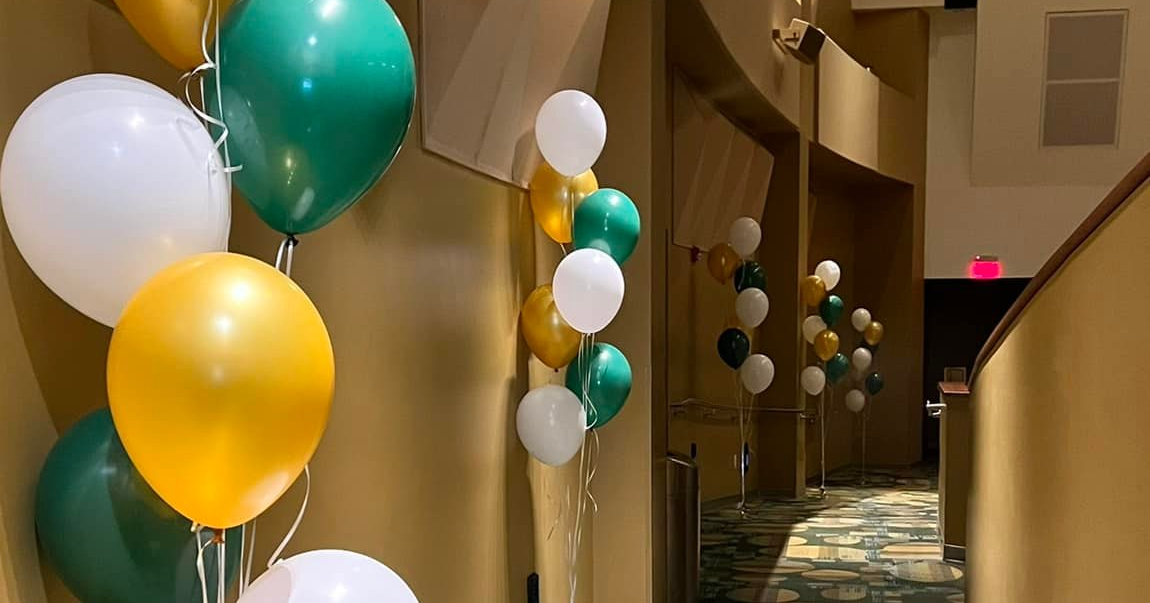 A hallway filled with green , yellow , and white balloons.