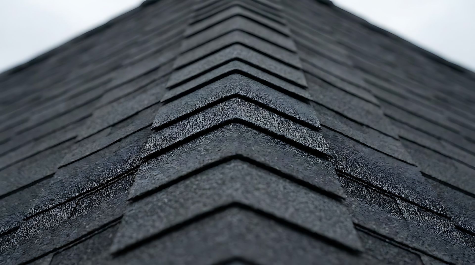 Close-up of dark gray roof shingles with a central ridge line Close-up of dark gray roof shingles with a central ridge line