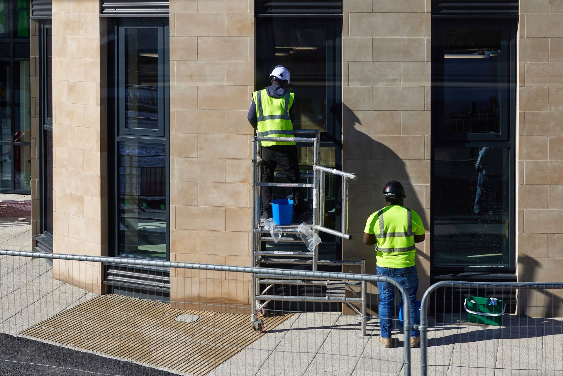 Two workers in neon safety vests on scaffolding cleaning a stone building facade