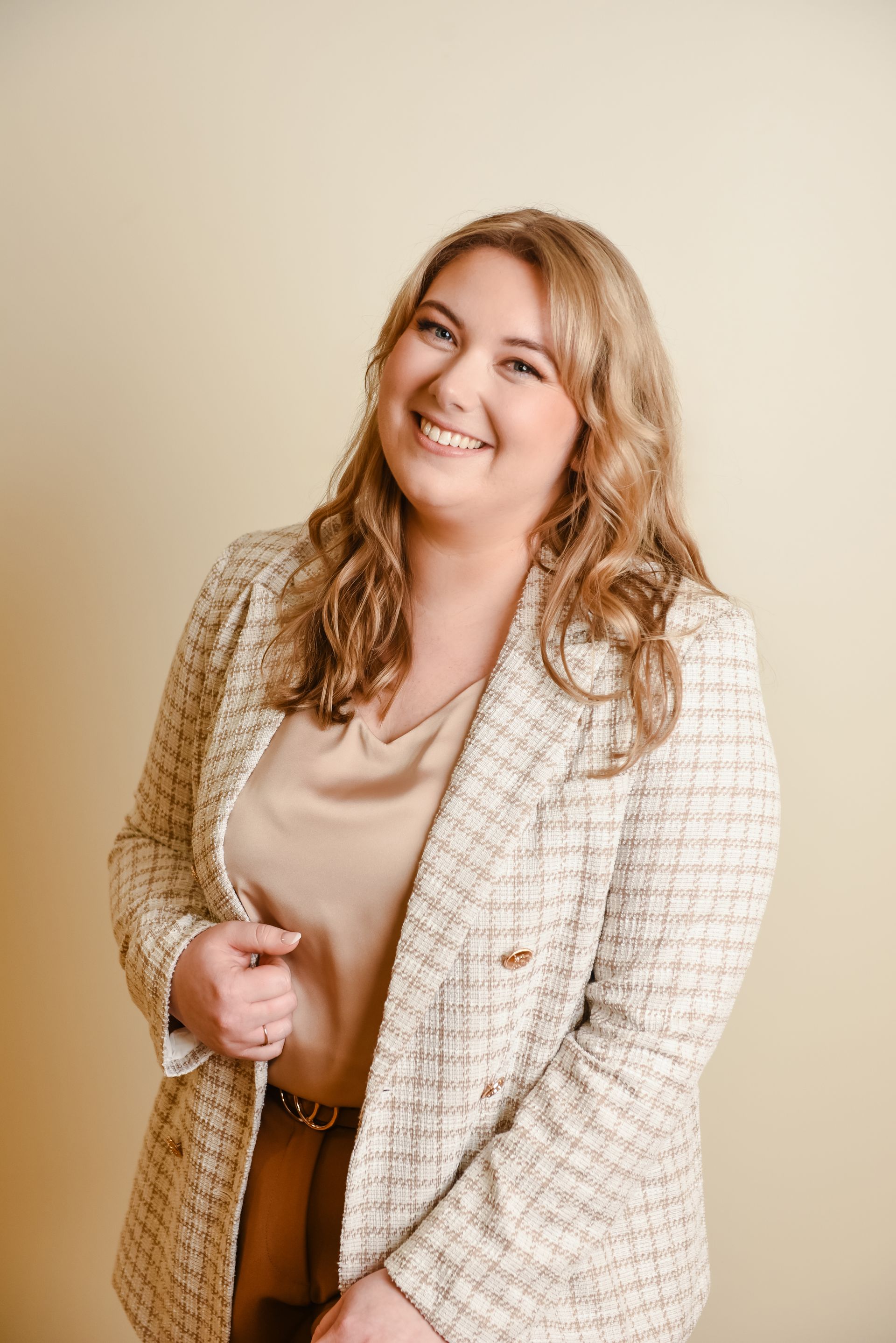 A smiling person wearing a textured cream blazer over a neutral top, posing against a solid light background.