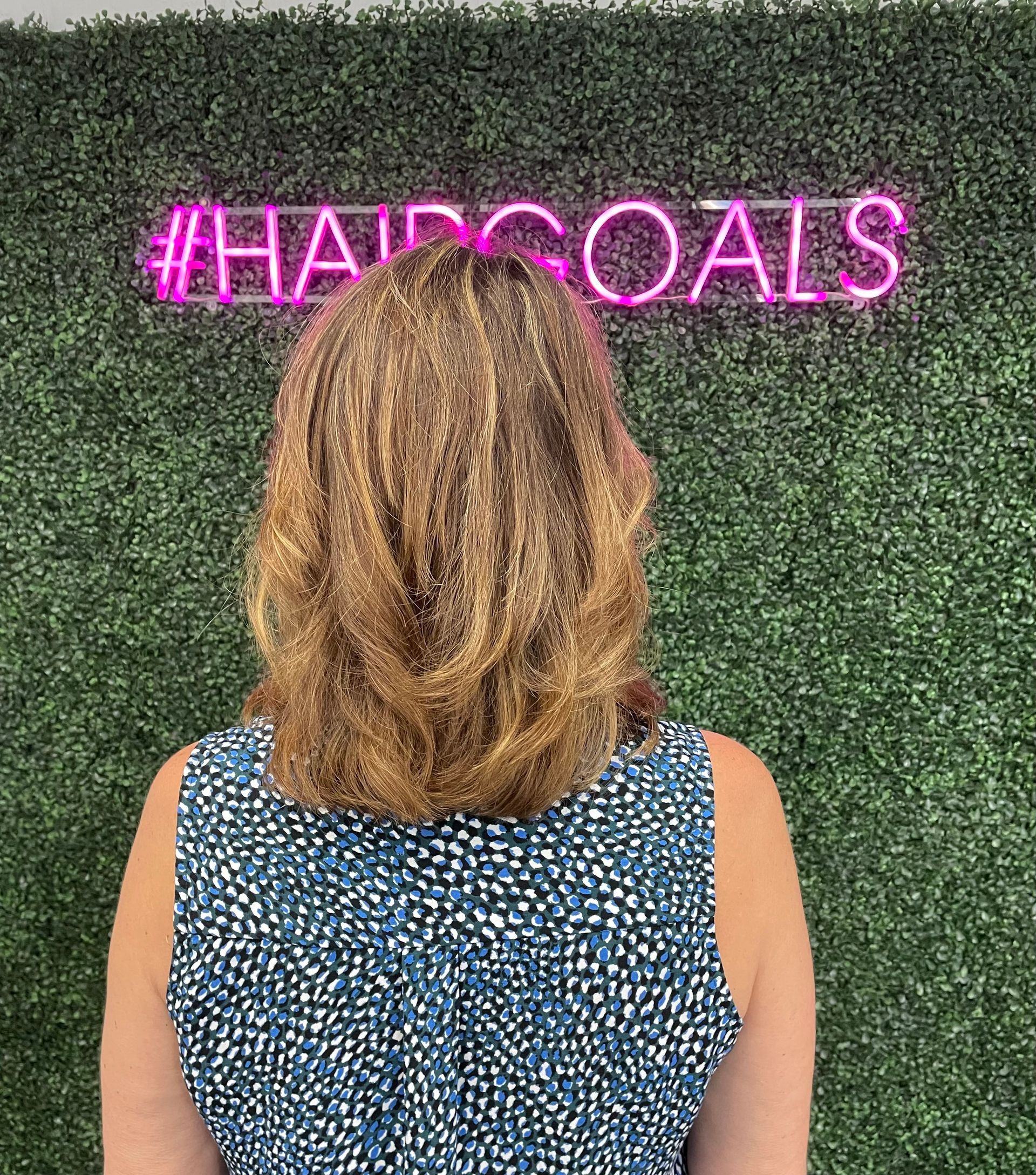 A woman in a blue dress is standing in front of a neon sign.