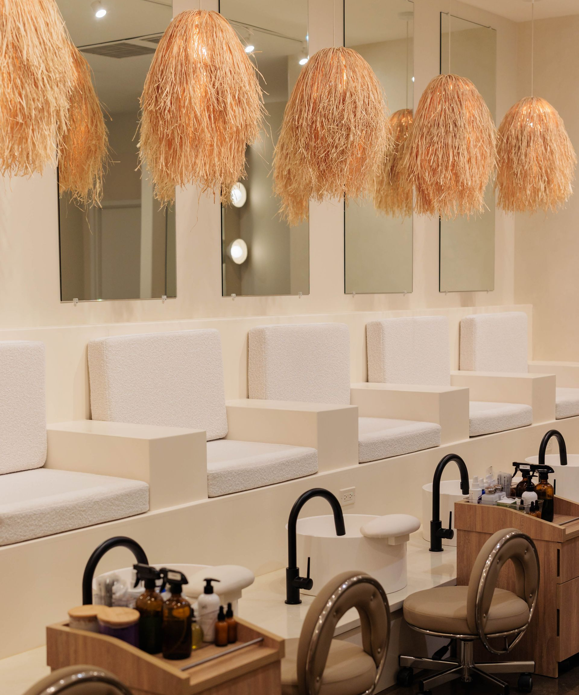 A clean, minimalist nail salon with white cushioned chairs, black fixtures, and decorative hanging straw light fixtures.